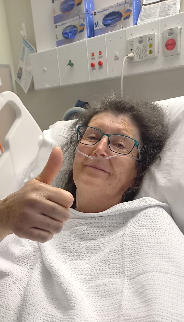 A woman laying in a hospital bed giving a thumbs up.