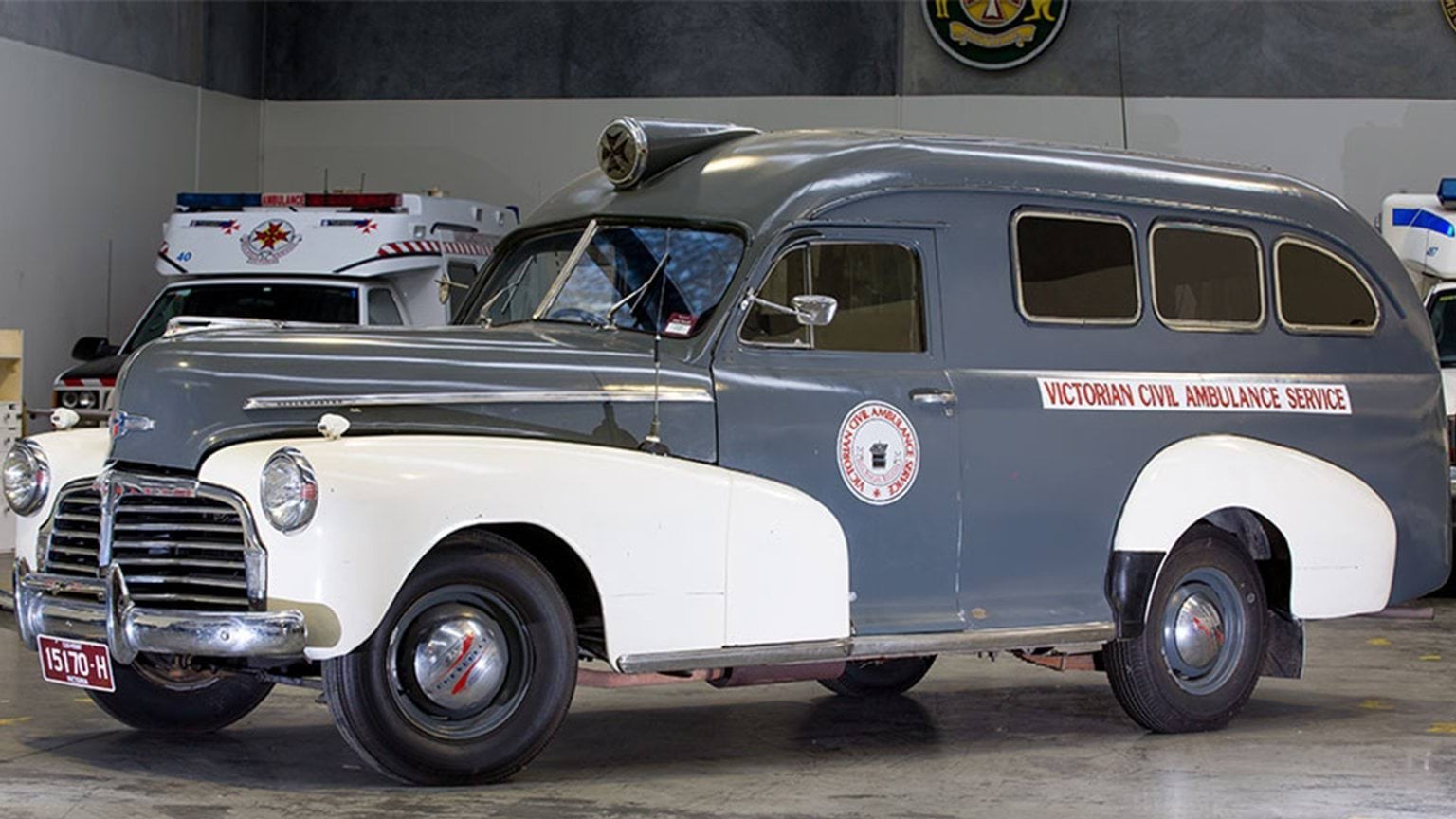A vintage grey and white ambulance parked inside a garage.