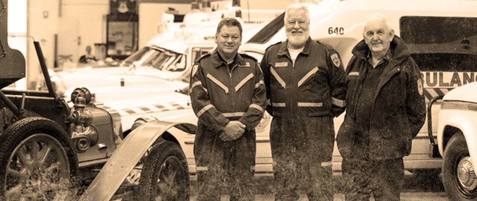 Ambulance Victoria Chas Martin OAM Museum Three retired paramedics and first responders standing in front of several vintage ambulance vehicles parked inside a garage.