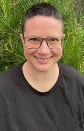 A woman with short hair and glasses smiles at the camera