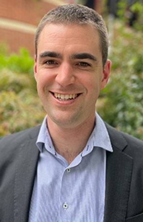 A man in a shirt and suit jacket smiles at the camera