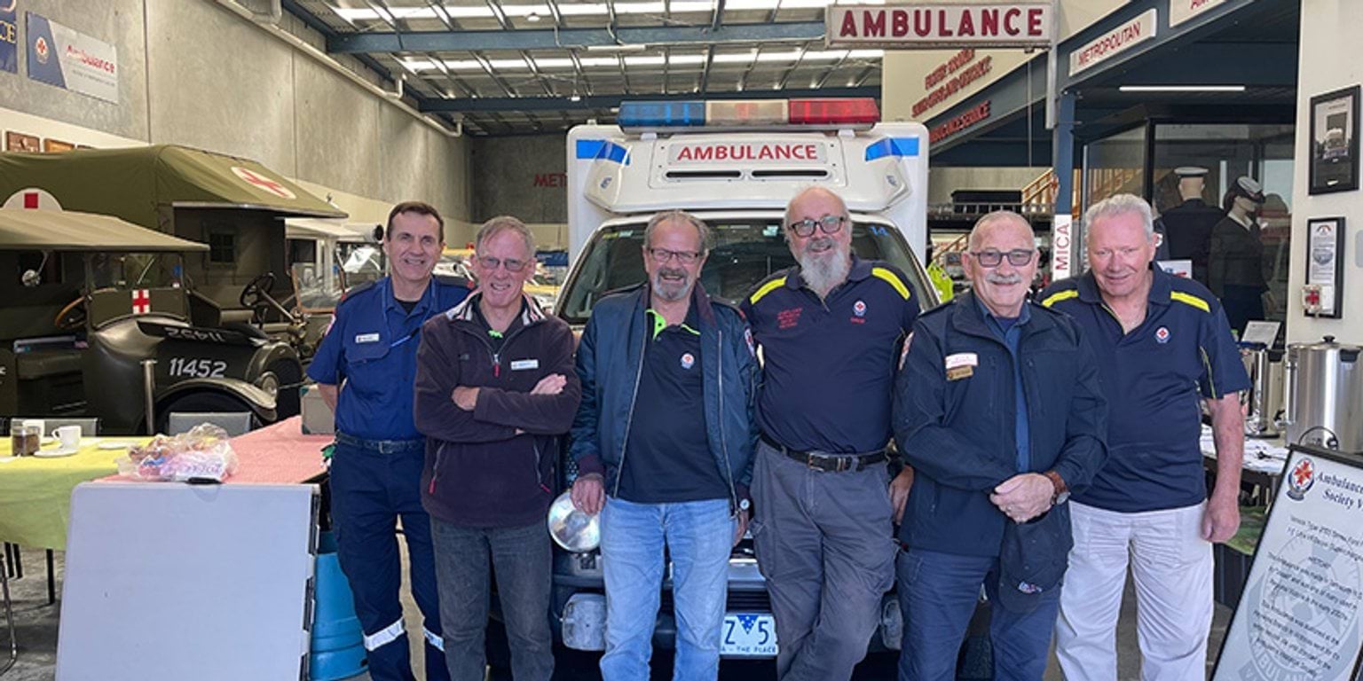 Ambulance Victoria Museum's volunteers standing together in front of a vintage ambulance.
