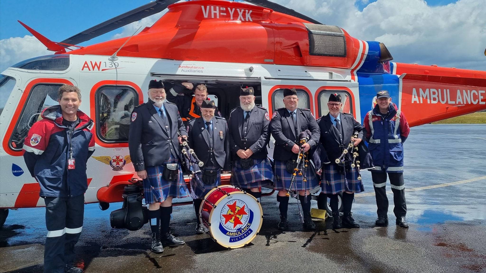 Members of the AV Pipes and Drums stand beside an AV helicopter