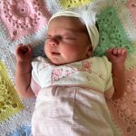 A newborn baby lies on a crochet blanket
