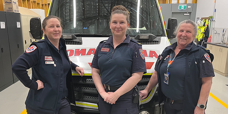 Three smiling female paramedics standing in front of an ambulance.