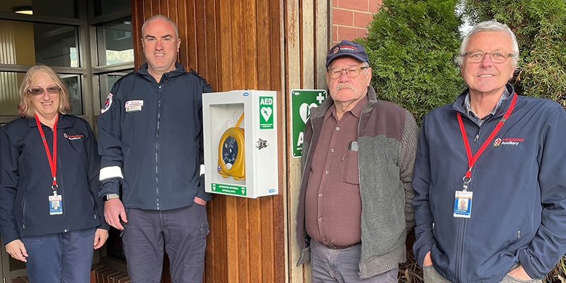 Three males and one female of the Baw Baw auxiliary team standing beside a new installed automated external defibrillators at the Warragul Ambulance Branch.
