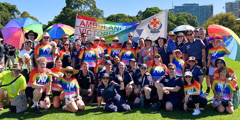 A group of Ambulance Victoria staff celebrating IDAHOBIT in a park while wearing clothing in pride colours.