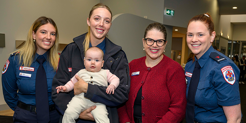 Ambulance Victoria's Chief Executive standing with three female paramedic graduates. One of the female paramedic graduate is holding an infant.