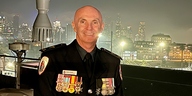 A profile shot of Eddie Wright with a city skyline as the background. he is wearing a uniform adorned with several medals.
