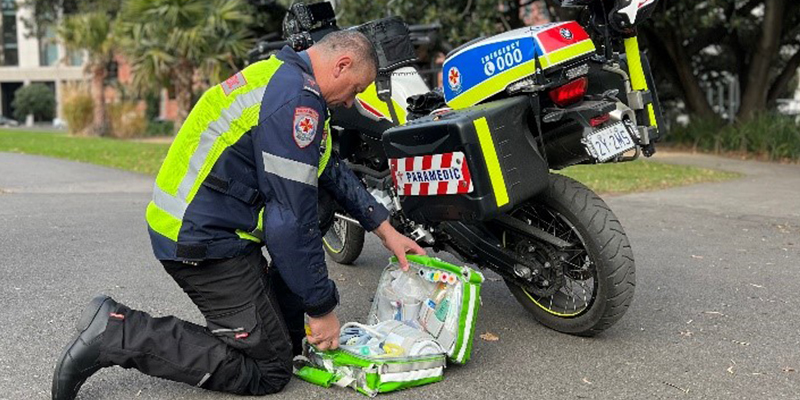A paramedics kneeling next to a motorcycle on the ground and arranging his gear and medication in a bag.