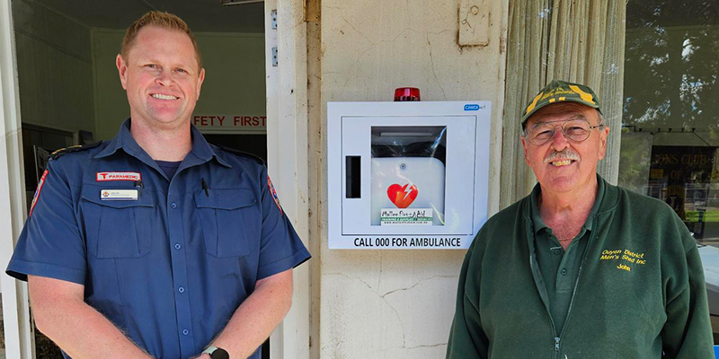 Two men standing in front of a newly installed automated external defibrillator device.