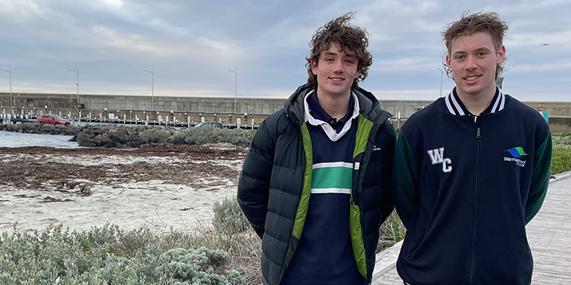 Two young men standing on a boardwalk near the water.