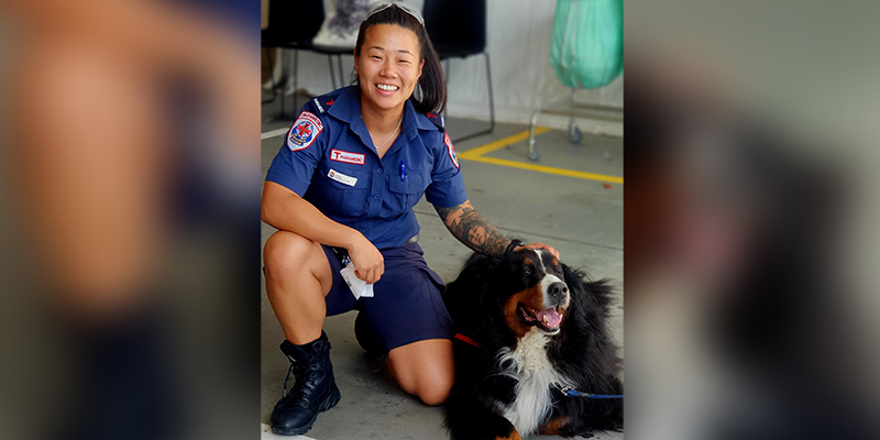 A female paramedic in blue uniform kneeling and petting a service dog.