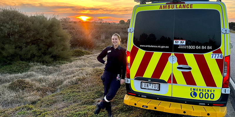 A woman leaning next to a ambulance with a sunset in the background.