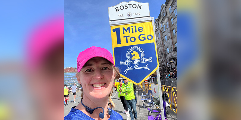 A female runner standing beside a race distance marker in the city of Boston.