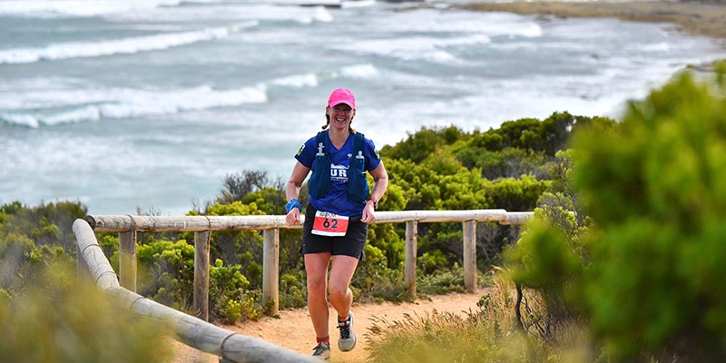 A female runner running on a trail along the coast with the sea in the background.