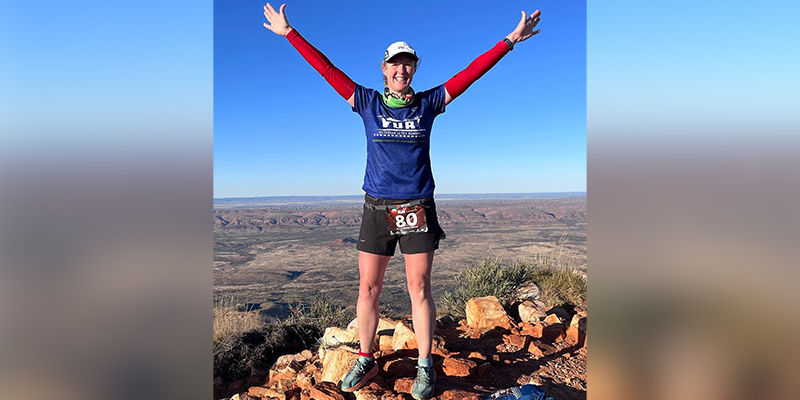 A female runner standing on some rocks with her arms stretch out into the air.