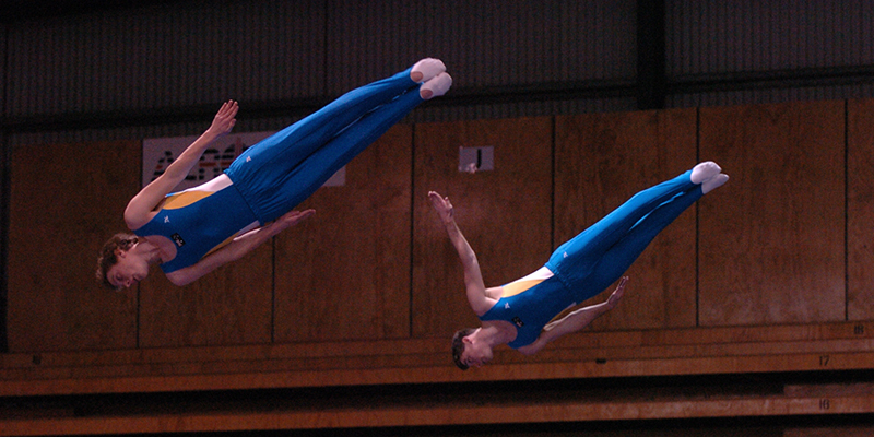 Two athletes performing an acrobatic trick on a trampoline, showcasing their athleticism and coordination in mid-air.
