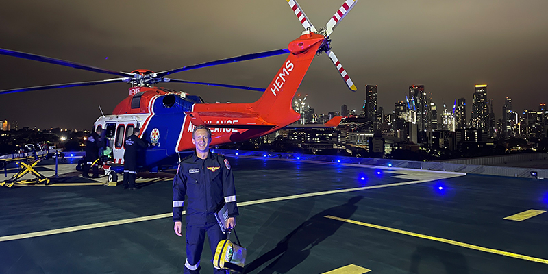 A paramedic standing by an ambulance helicopter parked on a helipad on top of a building with a city skyline in the background.