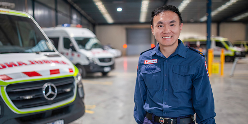A man in blue uniform standing in front of ambulances inside a garage.