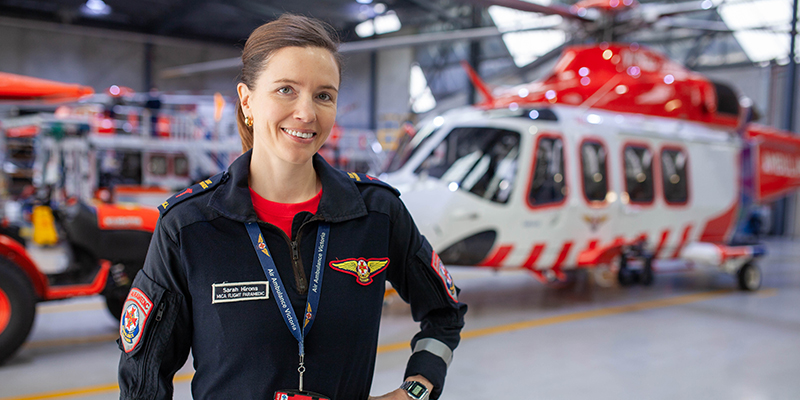 A female in a black and red uniform standing in front of a helicopter inside a hangar.