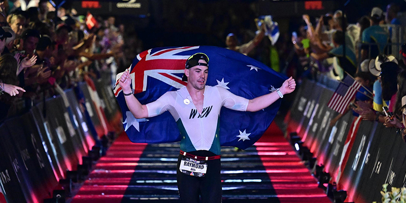 An athlete running through the finishing line while holding the Australian flag.