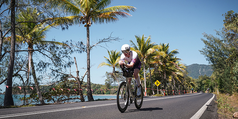 A racer riding a bicycle on a long stretch of road by the coast.