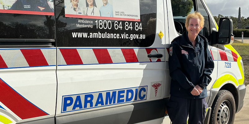 A female paramedic standing next to an ambulance parked in front of a house.