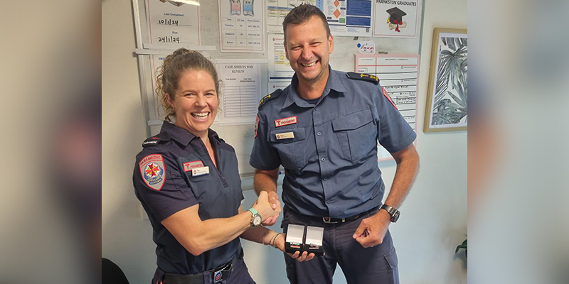 A female paramedic in blue uniform shaking hands with a male paramedic while receiving medals.