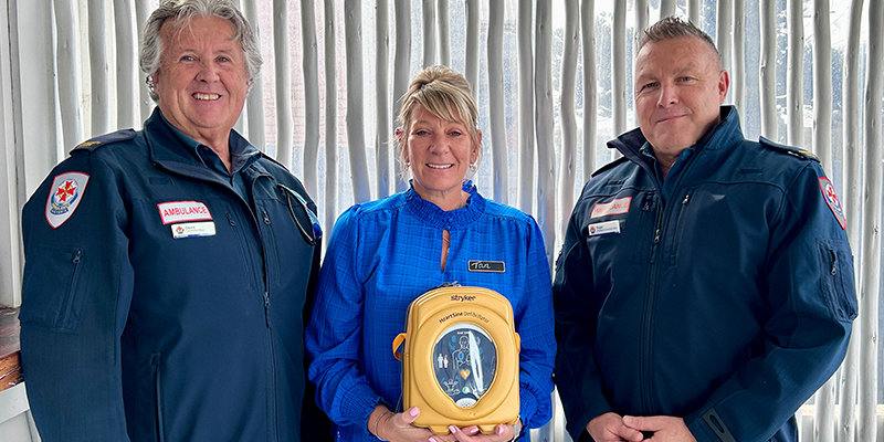 Three people standing together and one person is holding the Automated External Defibrillator device.