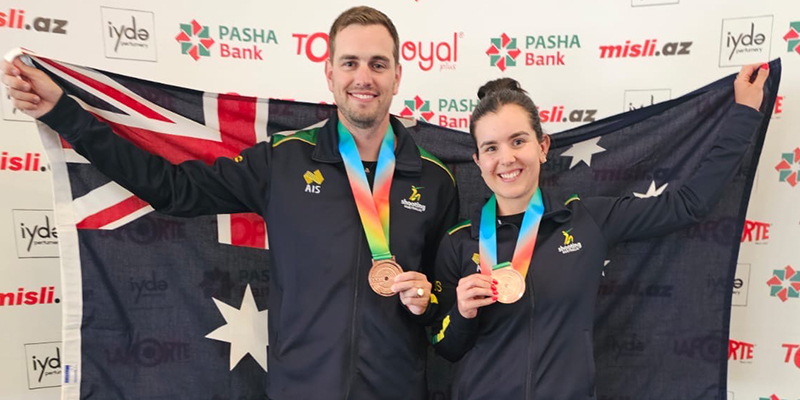 Two people proudly holding medals in front of an Australian flag.