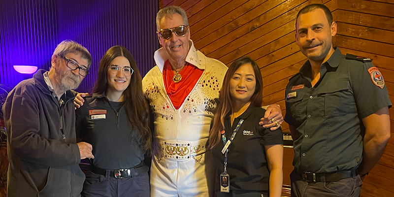 An Elvis impersonator posing with four people in a recording studio.