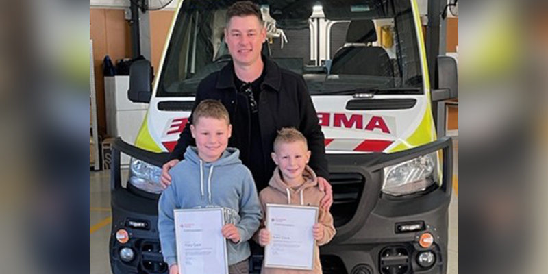 A man and two children proudly display certificates in front of an ambulance.