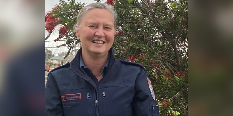A female paramedic in blue jacket standing in a garden.
