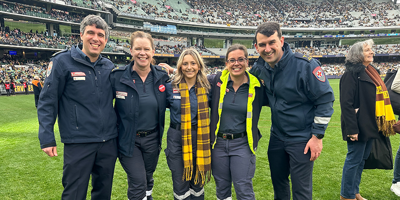 A group of five people in paramedic uniform standing together on a grassy field in the middle of a crowded stadium.