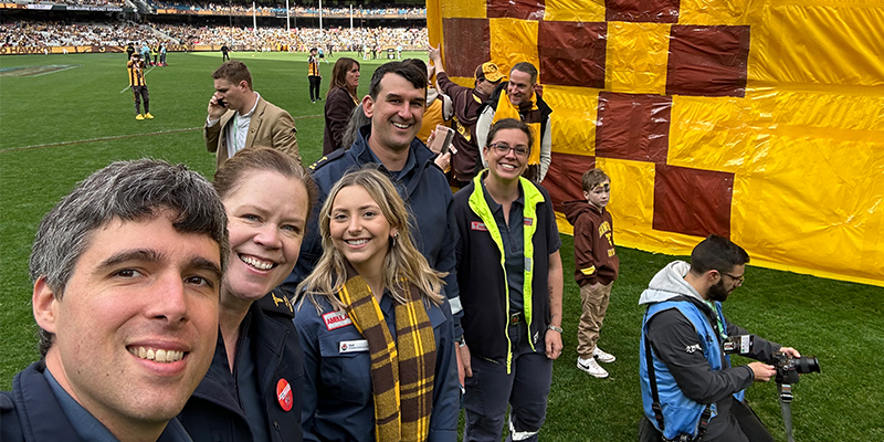 A group of five individuals in paramedic uniform standing on the grassy field in the middle of a packed stadium.