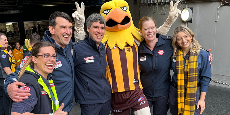 Five individuals in paramedic uniform standing together with a sport mascot that resembles a hawk.