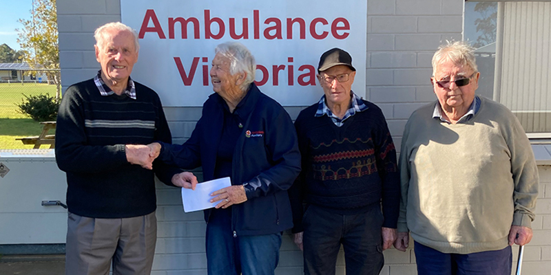 Four men are standing on the side of a building with an Ambulance Victoria signage on the wall.