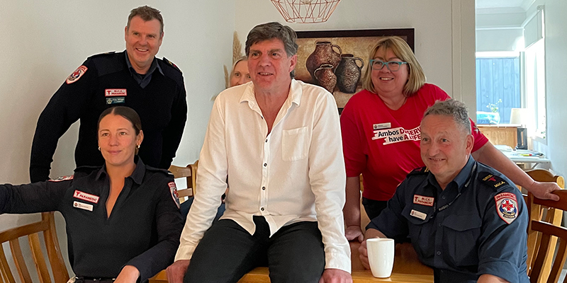 Six people are seated at a dining table inside a house. One man is sitting on the table.