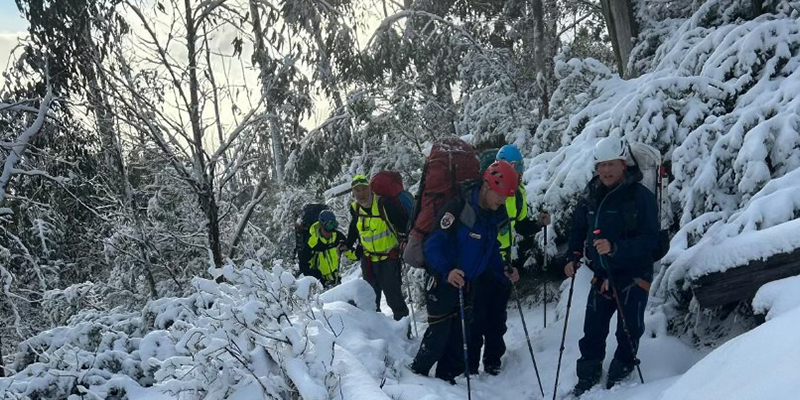 A group of rescuers hiking on a trail covered with thick snow.