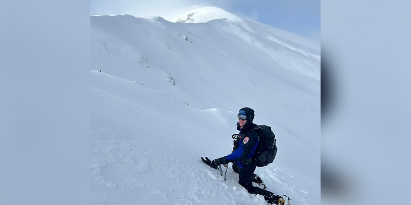 One male rescuer kneeling on a slope of a snowy mountain.