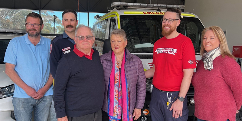 Six people are standing in front of an ambulance.