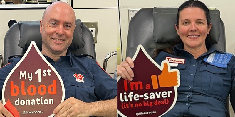 A male and a female paramedic sitting on a couch while holding up a blood donation sign.