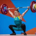 A woman lifting a loaded barbell over her head during a weightlifting competition.