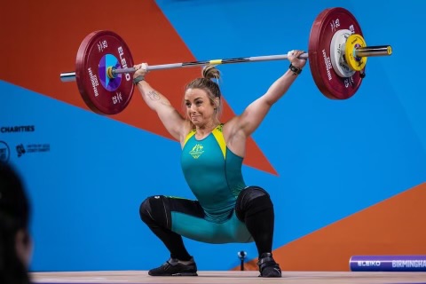 A woman lifting a loaded barbell over her head during a weightlifting competition.