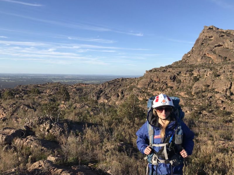 A woman paramedic in wilderness response uniform standing in a bush landscape.