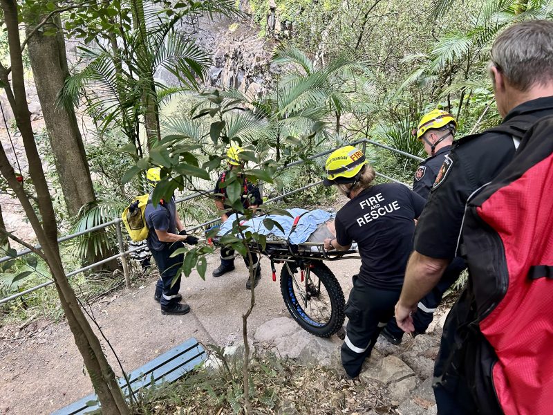 Queensland Fire and Rescue workers transport a stretcher down steps on a trail.