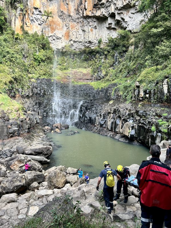 Rescue workers transport a stretcher near a waterfall.