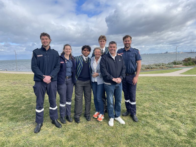 Paramedics and a family smile together on the grass in front of Elwood Beach.