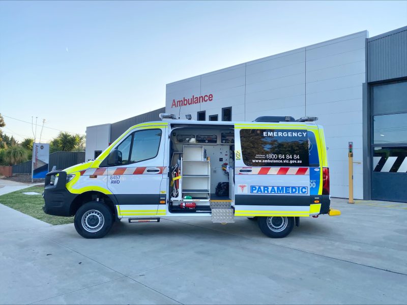 An all-wheel-drive ambulance vehicle with the side door open, parked in front of an Ambulance Victoria branch.